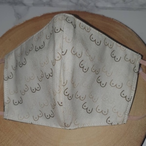 May include: A white face mask with a repeating pattern of brown and beige stylized breasts.