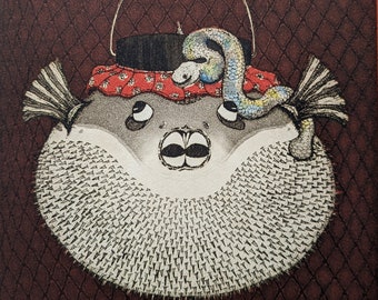 May include: A black and white illustration of a pufferfish with a red and white bandana and a blue and green snake wrapped around its head. The fish is hanging from a string.