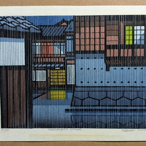 Könnte beinhalten: Ein künstlerischer Druck einer japanischen Straßenecke mit Gebäuden mit braunen, blauen und weißen Fassaden. Das Kunstwerk hat ein vertikales Linienmuster, mit einem gelb und grün beleuchteten Fenster. Der Druck ist signiert und mit 35/50 nummeriert.