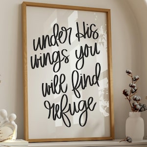 Pode incluir: Uma impressão emoldurada com as palavras "under His wings you will find refuge" em escrita preta. A impressão é exibida em um armário branco, com elementos decorativos, incluindo plantas secas e um vaso branco com caules de algodão.