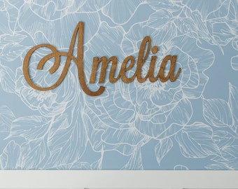 May include: White crib with a pink and white crocheted blanket with a daisy pattern. The crib is in front of a blue wall with a white floral pattern and the name "Amelia" written in wood letters.