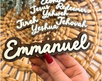 May include: Wooden ornaments with the names "Emmanuel", "Counselor", "Elohim", "Jesus", "Redeemer", "Yahweh", "Jireh", "Yeshua", and "Jehovah" in white script on a dark wood background. The ornaments are layered with a light wood backing.