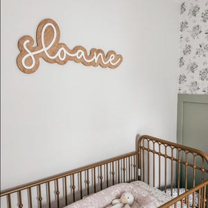 Custom wooden nursery name sign on wood backer with the name "Sloane" in a white script font.