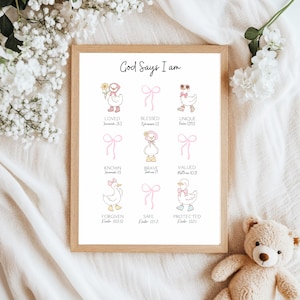 May include: A framed print with the text "God Says I am" and illustrations of ducks with bows. The print includes words like "Loved," "Blessed," and "Unique," with corresponding Bible verses. The frame is light brown.