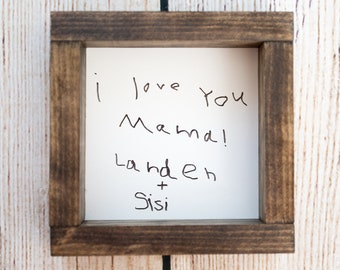 May include: A framed handwritten note that reads "I love you Mama! Laden + Sisi" in black ink on white paper.