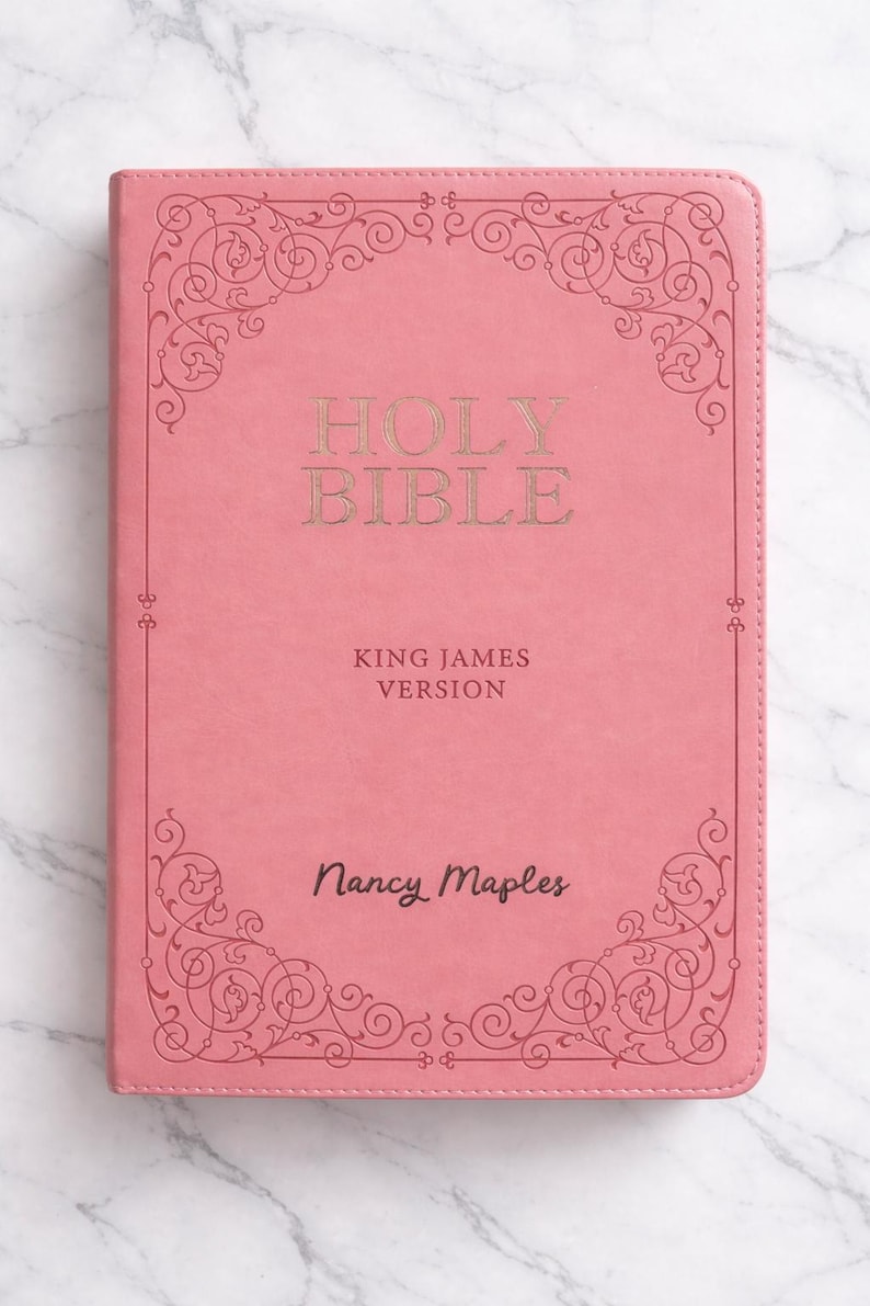 Pu&ograve; includere: Bibbia rosa con scritte dorate e decorazioni angolari. La copertina recita "Holy Bible, King James Version" e "Nancy Maples". Il libro &egrave; ambientato su uno sfondo di marmo.