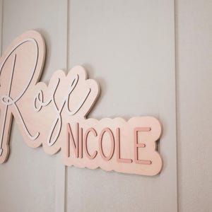 Outline custom nursery name sign with the name Rose Nicole in white and pink on natural wood backer