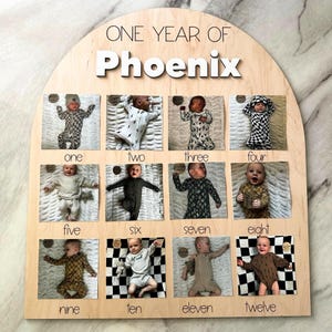 K&ouml;nnte beinhalten: Holz-Fotodisplay-Board mit dem Text "ONE YEAR OF Phoenix". Das Board verf&uuml;gt &uuml;ber zw&ouml;lf Fotoschlitze, die jeweils mit einem Monat von eins bis zw&ouml;lf beschriftet sind. Jeder Schlitz enth&auml;lt ein Babyfoto, das das erste Jahr des Babys dokumentiert.