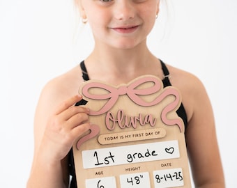 Peut inclure: Panneau en bois avec un nœud rose en haut, personnalisé avec le nom "Olivia". Le panneau indique "1st grade", âge 6, taille 122 cm, et la date 8-14-25. Il liste également "Vétérinaire" comme aspiration future et "Licornes, sirènes, la terre" comme choses préférées.