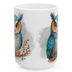 May include: White ceramic mug featuring a detailed illustration of a blue and orange owl perched on a branch with orange flowers. The owl has large yellow eyes and is set against a soft gray background.