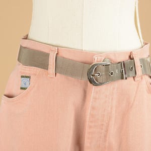 May include: A pair of light pink denim pants with a silver buckle belt. The belt is a woven mesh material.