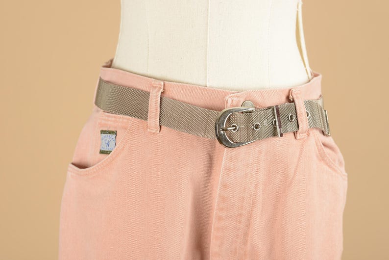 May include: A pair of light pink denim pants with a silver buckle belt. The belt is a woven mesh material.