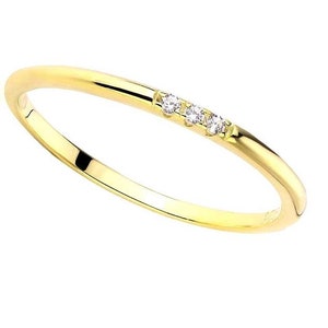 May include: A delicate gold ring with three small, clear gemstones set in a row. The ring has a smooth, polished band and a simple, elegant design. The ring is a size O.