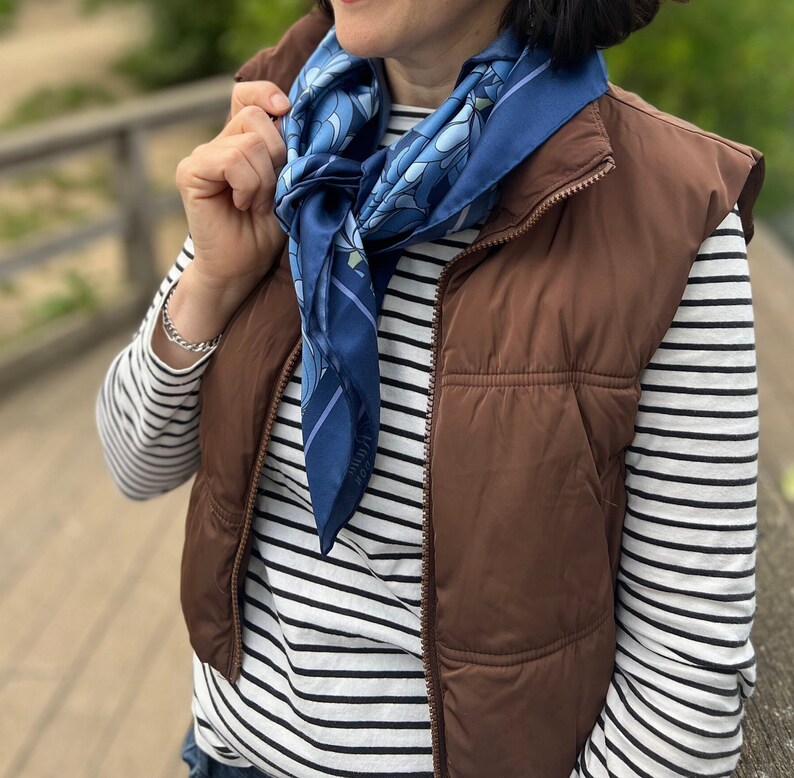 Tied around the neck, the floral motif silk scarf is complete with a vibrant floral abstract print and wide purple border with hand rolled edges on a deep purple base.