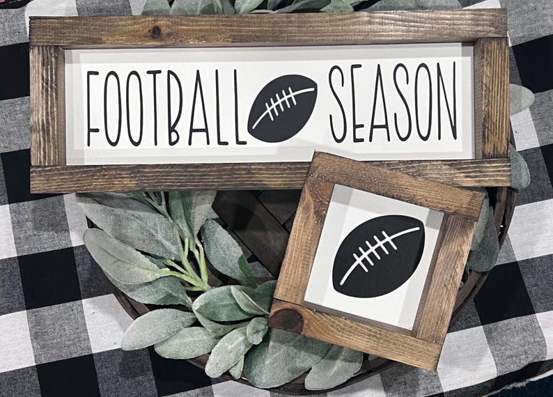 May include: Two rectangular wooden signs with dark brown frames and white centers. The larger sign features the black text FOOTBALL SEASON with a football icon. The smaller square sign features a single black football icon in the center.