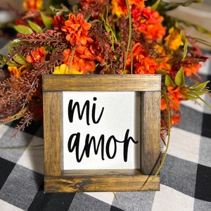 May include: A wooden framed sign with the words "mi amor" written in black on a white background. The sign is sitting on a black and white checkered surface.