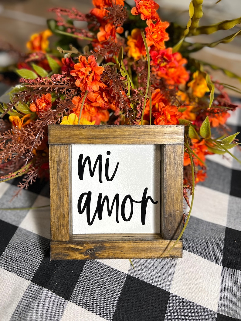 May include: A wooden framed sign with the words "mi amor" written in black on a white background. The sign is sitting on a black and white checkered surface.