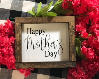 May include: A rustic wooden framed sign with the text "Happy Mother's Day" in black calligraphy on a white background. The sign is surrounded by pink flowers.