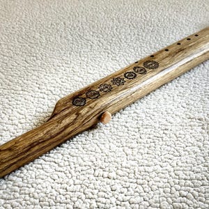 May include: A wooden flute with a brown leather strap and a series of symbols carved into the wood. The flute is approximately 24 inches long.