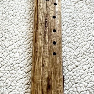 May include: A wooden flute with seven holes and a decorative design of seven chakras. The flute is made of dark wood with a light wood inlay at the bottom. The flute is decorated with a mother of pearl inlay.
