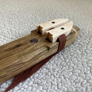 May include: A wooden flute with a brown leather strap and two wooden tuning keys with black dots. The flute is made of dark wood with a natural grain.