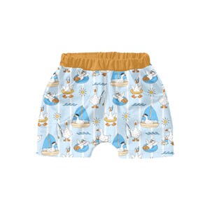May include: Light blue shorts with a repeating pattern of cartoon geese in sunglasses, on sailboats, and in inner tubes. The shorts have a yellow waistband and are made of a soft fabric.