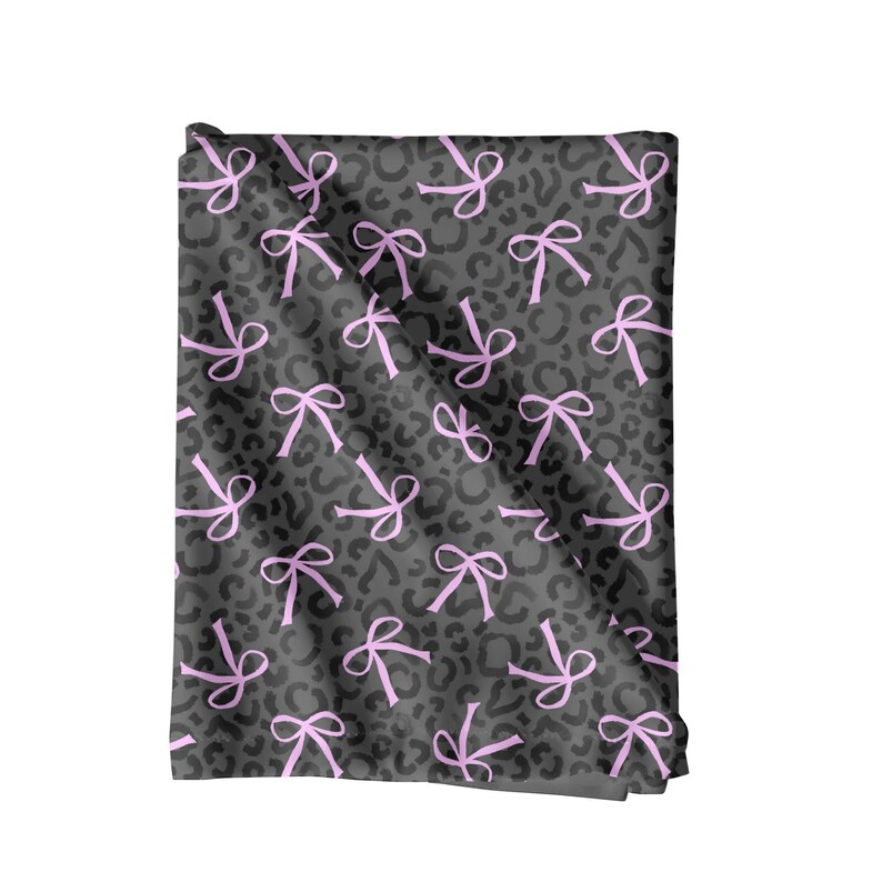 May include: A folded textile featuring a grey leopard print with a repeating pattern of pink bows. The bows are evenly distributed across the fabric. The material appears soft and could be used for various craft projects or as a decorative item.