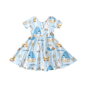 May include: A light blue dress with a pattern of white geese in boats, fishing, and swimming. The dress has short sleeves and a flared skirt. The background features vertical white stripes, suns, and waves.