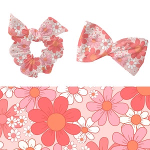 Op de afbeelding: Een roze en witte bloemenprint scrunchie en strik. De print heeft roze en witte madeliefjes op een lichtroze achtergrond.