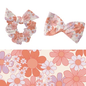May include: A pink and white floral print scrunchie and bow tie. The print features a repeating pattern of pink and white daisies.