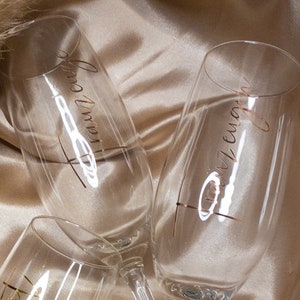 May include: Three champagne flutes with gold lettering. The flutes are on a beige fabric background. The lettering on the flutes reads "Forever", "Always", and "Together".
