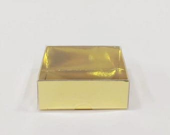 May include: A small, square, gold-colored box with a shiny finish. The box is empty and open.