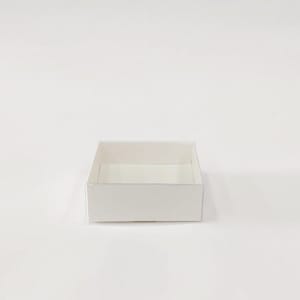 May include: A small, square, white cardboard box with a shallow depth. The box is empty and sits on a white surface. The box has a simple, clean design.