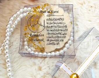 May include: A clear box with a white ribbon and gold accents contains a pearl necklace and a decorative piece with Arabic text and the words "Ayat ul Kursi" and "Ramadan Mubarak".
