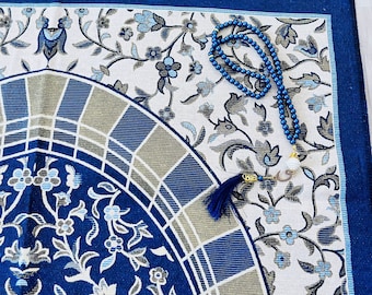 May include: A blue and white prayer rug with a floral pattern and a blue prayer bead necklace with a tassel.