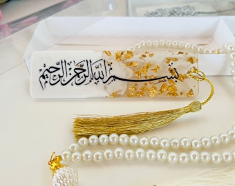 Peut inclure: Un marque-page blanc et or avec la phrase arabe "Bismillah Al-Rahman Al-Rahim" et un pompon doré. Le marque-page est associé à un chapelet de perles blanches avec un pompon doré.