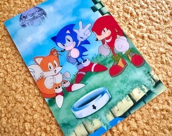 May include: A blue, red, and orange cartoon character illustration with a blue ring in the foreground. The characters are Sonic the Hedgehog, Tails, and Knuckles. The text "ソニックぷりズム" is in the top left corner of the image.