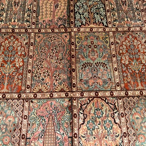 May include: Close-up of a detailed, patterned rug with a repeating design. The rug features a variety of colors, including red, pink, green, and beige. The pattern includes stylized trees and floral motifs, creating a symmetrical and ornate appearance.