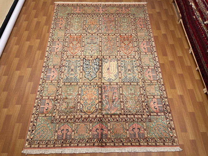 May include: An ornate, rectangular rug with a detailed, repeating pattern in shades of beige, pink, green, and orange. The design features floral and geometric motifs, creating a traditional aesthetic. The rug is displayed on a wooden floor.