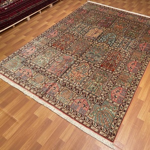 May include: A large rectangular rug with a detailed, repeating pattern of floral and geometric designs in shades of red, green, and beige. The rug has a cream-colored fringe along the edges and is displayed on a wooden floor.