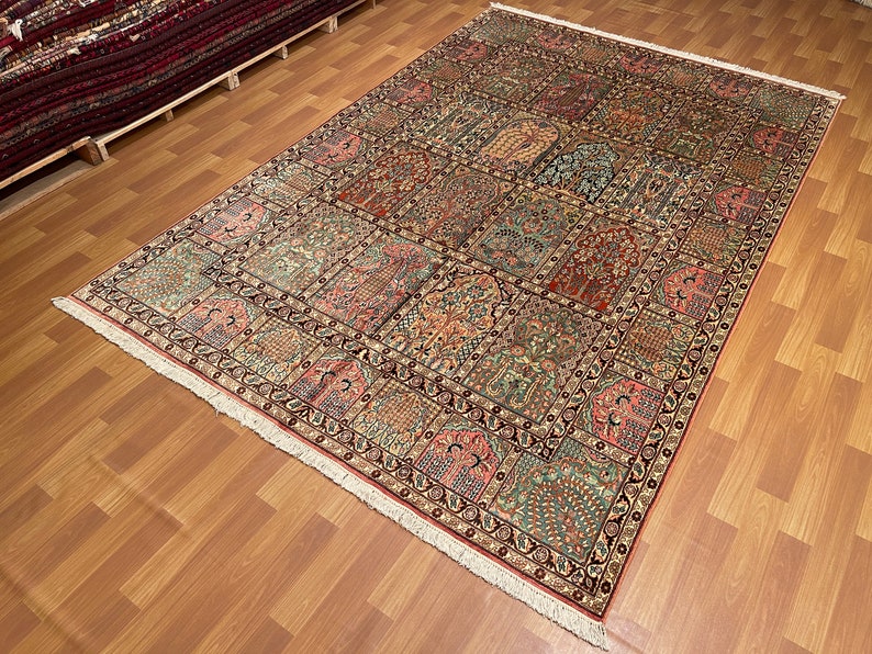 May include: A large rectangular rug with a detailed, repeating pattern of floral and geometric designs in shades of red, green, and beige. The rug has a cream-colored fringe along the edges and is displayed on a wooden floor.