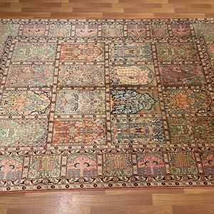 May include: An intricately designed rectangular rug with a repeating pattern of rectangular panels. The rug features a variety of colors, including shades of pink, green, and brown. The edges are bordered with a dark red and black pattern, and the rug has a fringe.