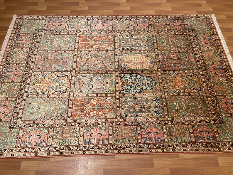 May include: An intricately designed rectangular rug with a repeating pattern of rectangular panels. The rug features a variety of colors, including shades of pink, green, and brown. The edges are bordered with a dark red and black pattern, and the rug has a fringe.