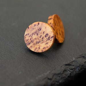 May include: A pair of round wooden earrings with a natural wood grain pattern and purple streaks. The earrings are approximately 2.5 cm in diameter.