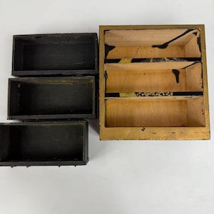 May include: A collection of small, rectangular wooden boxes. Three are black, and one is a multi-compartment box with a gold-painted exterior and decorative black and gold accents. The boxes are empty and appear to be vintage.