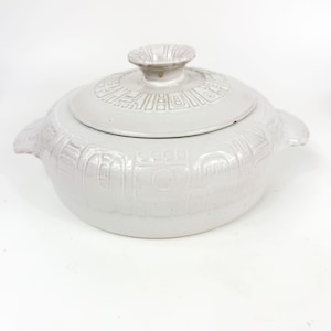 May include: A light gray ceramic casserole dish with a lid. The dish has a rounded shape with two handles and a decorative pattern. The lid has a knob and a matching pattern. The dish is suitable for cooking and serving.