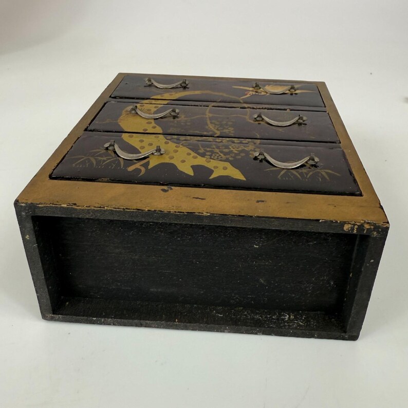 May include: A small, three-drawer wooden chest with a black exterior and gold trim. The drawers are black with gold and yellow bird and floral designs. Each drawer has a small, silver-colored handle.