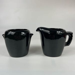 May include: A black ceramic creamer and sugar bowl set. The creamer has a rounded spout and a handle. The sugar bowl has a rounded shape with a lid.