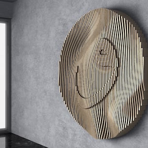 Op de afbeelding: Een groot, rond houten wandkunstwerk met een smiley-gezicht ontwerp. De kunst is gemaakt van verticale houten latten die een golvend, gestructureerd oppervlak creëren. Het stuk is gemonteerd op een grijze betonnen muur, met een raam zichtbaar op de achtergrond.