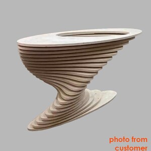 May include: A wooden table with a unique, swirling design. The table is made of multiple layers of wood that are stacked and curved to create a unique shape. The table has a round top and a base that is shaped like a wave.